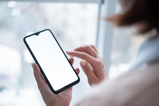 Woman holding phone with blank screen in hand on street view from window background