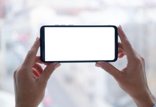 Smartphone with active blank screen in woman hands on cityscape background