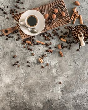 A cup of black coffee with candies and cinnamon sticks on a concrete background top view. View fron above. Copyspace area.