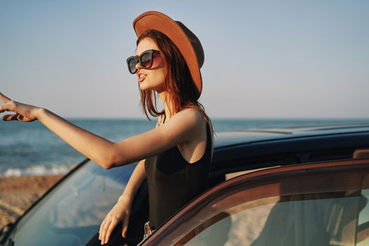 cheerful woman in sunglasses and a hat on the ocean near the car. High quality photo