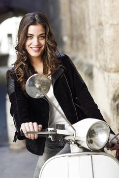 Woman in urban background smiling and wearing casual clothes with a old scooter in the background