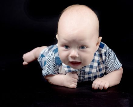 A charming baby lies on the blanket and looks into the camera on a black background. The concept of a happy childhood, the birth and upbringing of a child.