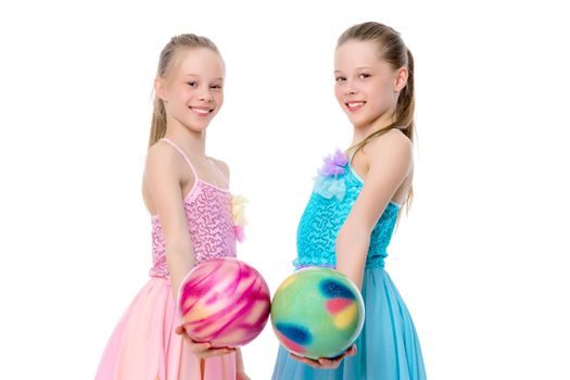 Two cheerful little girls gymnasts in competitions, perform exercises with the ball. The concept of children's sports, fitness, healthy lifestyle. Isolated on white background.