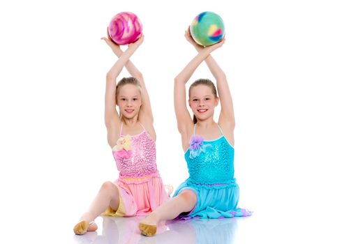 Two cheerful little girls gymnasts in competitions, perform exercises with the ball. The concept of children's sports, fitness, healthy lifestyle. Isolated on white background.