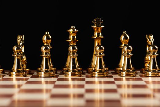 Golden chess figures standing on chessboard. Intellectual competition and fight in business. Strategy planning and leadership concept with copy space. Gold chess pieces in row on black background.