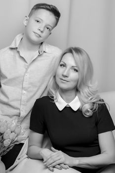 A beautiful young mother and son of school age near a bouquet of tulips, which the son gave his mother for a holiday. The concept of women's holiday, family values.Black and white photo.