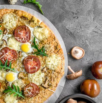 Homemade pizza with mushrooms and mozzarella decorated with arugula on a concrete background with food ingredients