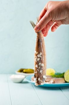 Female hand holding herring with onion, traditional dutch delicacy called hollandse nieuwe on turquoise background. European food concept with copy space.