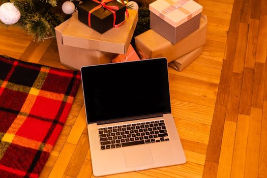 Christmas online shopping. Laptop with copy space on screen lay, present boxes and christmas tree on background. Internet commerce on winter holidays concept