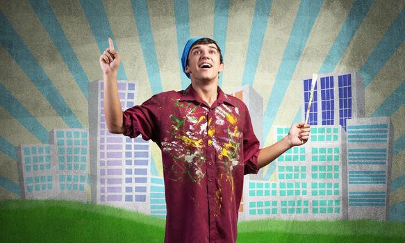 Young male artist holding paintbrush. Happy painter in shirt and bandana standing on background colorful picture on wall. Modern cityscape with high skyscrapers artwork. Creative hobby and profession