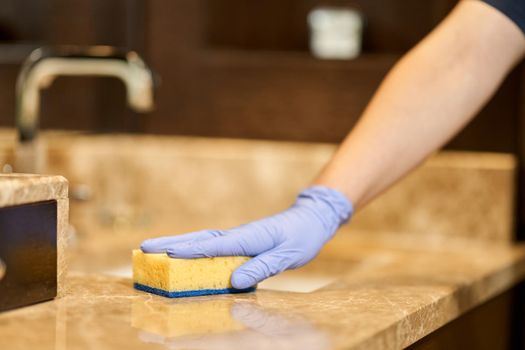 Close up of maid hand in a protective glove holding a washcloth and wiping the countertop. Hotel service concept