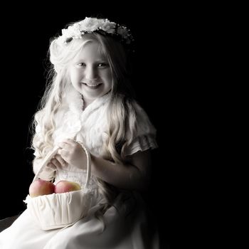 Little girl with a basket of apples. The concept of a healthy diet, happy childhood. On a black background.