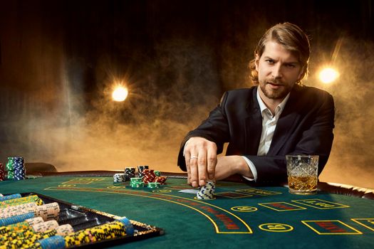 A man in a business suit sitting at the game table. Male player. Passion, cards, chips, alcohol, dice, gambling, casino - it is as male entertainment. Dangerous fun card game for money. Let the smoke.