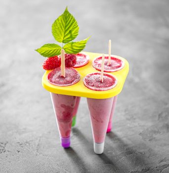 Cool homemade raspberry cones standing in a yellow ice cream container, decorated with leaves