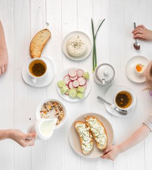 Family eating delicious breakfast together, toasts with cottage cheese and oatmeal, herbal tea, topview