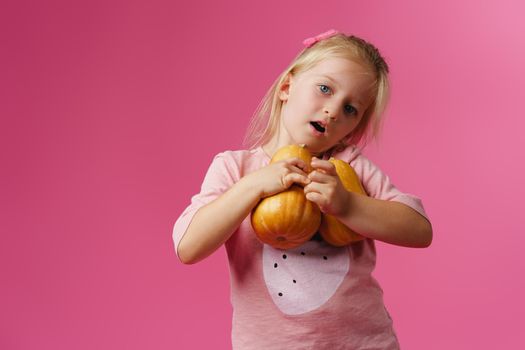 Little girl holding pumpkin in her hands against pink pastel background