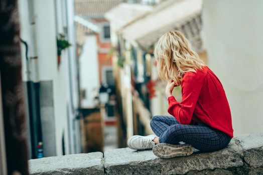 Young blonde tourist woman sitting outdoors looking a beautiful narrow street in Granada, Andalusia, Spain