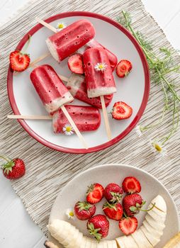 Homemade ice-cream from bananas and strawberries, cut bananas and berries on big white plate, topview