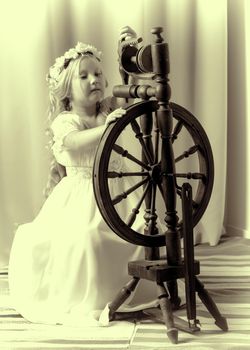 A cute little girl wove a wool with a rotating wheel. Retro style, memories of the past.