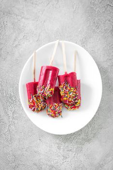 Lovely sprinkled popsicles made with red berries, red currant, raspberry ice-cream, served on plate, topview