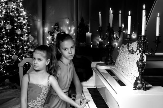 Lovely little girls on a Christmas night by candlelight near a white grand piano. Black and white photos. The concept of holidays, happy childhood.