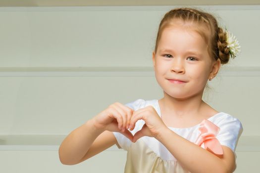 Beautiful little girl shows heart by hands. The concept of happy people, childhood.