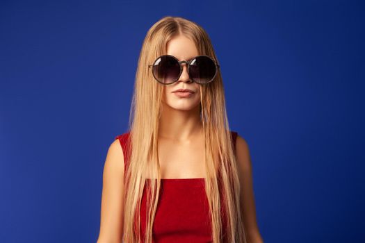 Young female model with long blond hair wearing stylish sunglasses against blue background