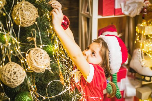 Cute child girl is decorating the Christmas tree. Kid decorating Christmas tree with bauble