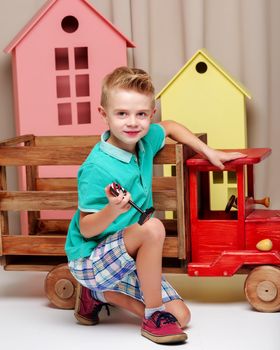 A cute little boy is playing with a big wooden car. The concept of development of a child in a family or a children's center. Advertising of children's goods and services. Isolated on white background.