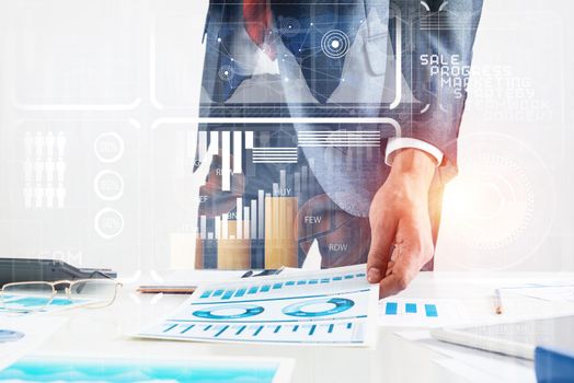 Businessman standing near office desk and analyzing financial charts. Successful corporate manager in business suit and tie. Close-up man hand with analytics. Entrepreneurship and leadership concept.