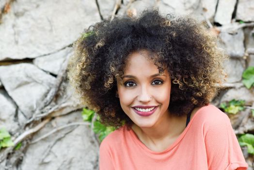 Mixed woman with afro hairstyle standing in an urban park. Young girl smiling.