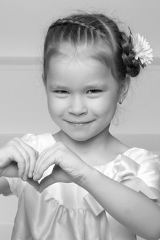 Beautiful little girl shows heart by hands. The concept of happy people, childhood.