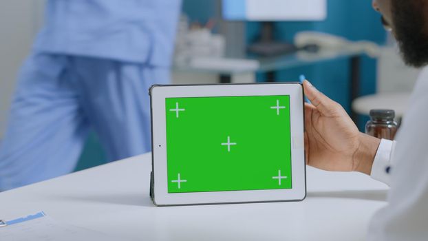 African american man analyzing medical expertise working at sickness report in hospital office. Mock up green screen chroma key tablet computer with isolated display. Medicine services