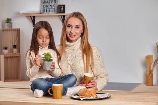 Caring mom. Nice smiling mother giving croissant to her child sitting on the kitchen