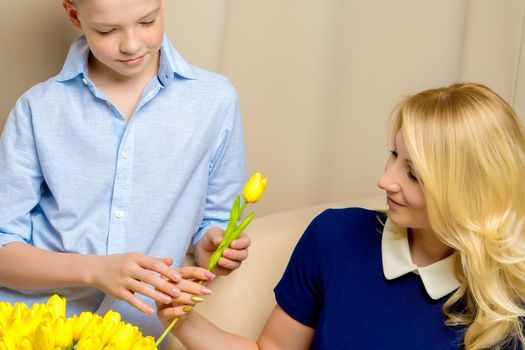 A beautiful young mother and son of school age near a bouquet of tulips, which the son gave his mother for a holiday. The concept of women's holiday, family values.