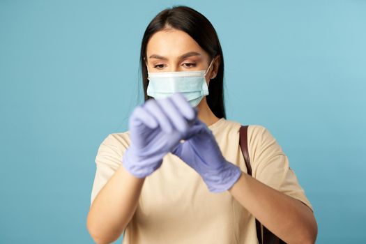 Serious woman wearing a disposable medical mask and wearing gloves during a pandemic, isolated on blue background. Copy space. Quarantine, epidemic concept