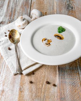 Delicious creamy mushroom soup with some pieces of mushrooms in it, old spoon and napkin