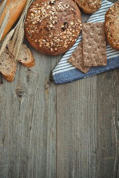 Different types of bread on a wooden table with ears of wheat