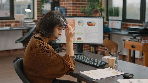 Contemplative woman working on rate charts design using computer and keyboard while looking at clipboard papers. Concentrated entrepreneur planning business project and presentation