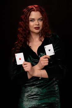 Young redheaded woman with curly hair and a playing cards in her arms over black. Win casino holdem poker slots