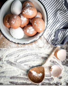 Empty eggshells and colorful eggs sitting on table sprinkled with flour, napkin nearby, topview