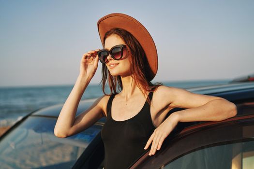 cheerful woman in sunglasses and a hat on the ocean near the car. High quality photo