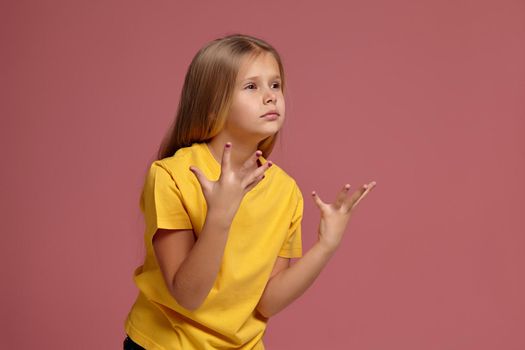 little girl in a yellow t-shirt on coral background. surprised shows hands