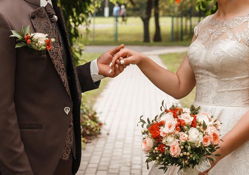 The groom in a brown suit holds the bride's hand with a wedding bouquet.