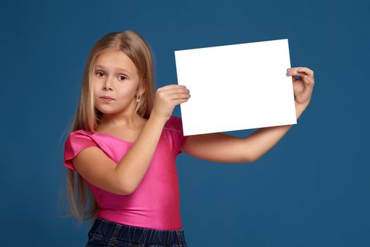Portrait of adorable blonde little girl on blue background. in pink shirt, holding horizontal white copy space aside her head