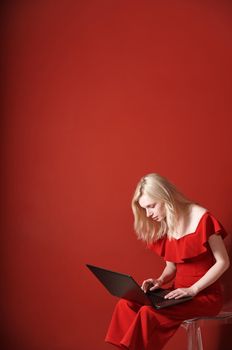 Young adult woman sitting on a chair and working on laptop