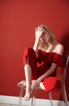Beautiful young adult woman wearing red jumpsuit relaxing on chair
