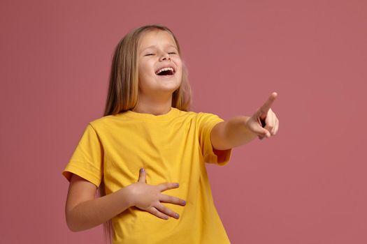 little girl in a yellow T-shirt on a coral background. laughs pointing finger