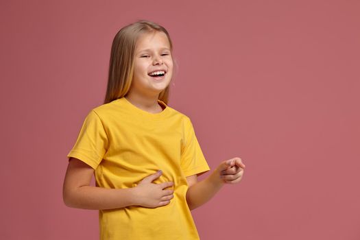 little girl in a yellow T-shirt on a coral background. laughs pointing finger