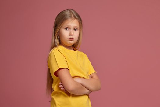 little girl in a yellow T-shirt on a coral background. looks offended